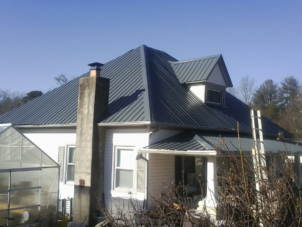 Dark blue standing seam metal roof on a white farmhouse with dormer — Slate & Tile Roof Repair by Roofing Brothers in Shortsville