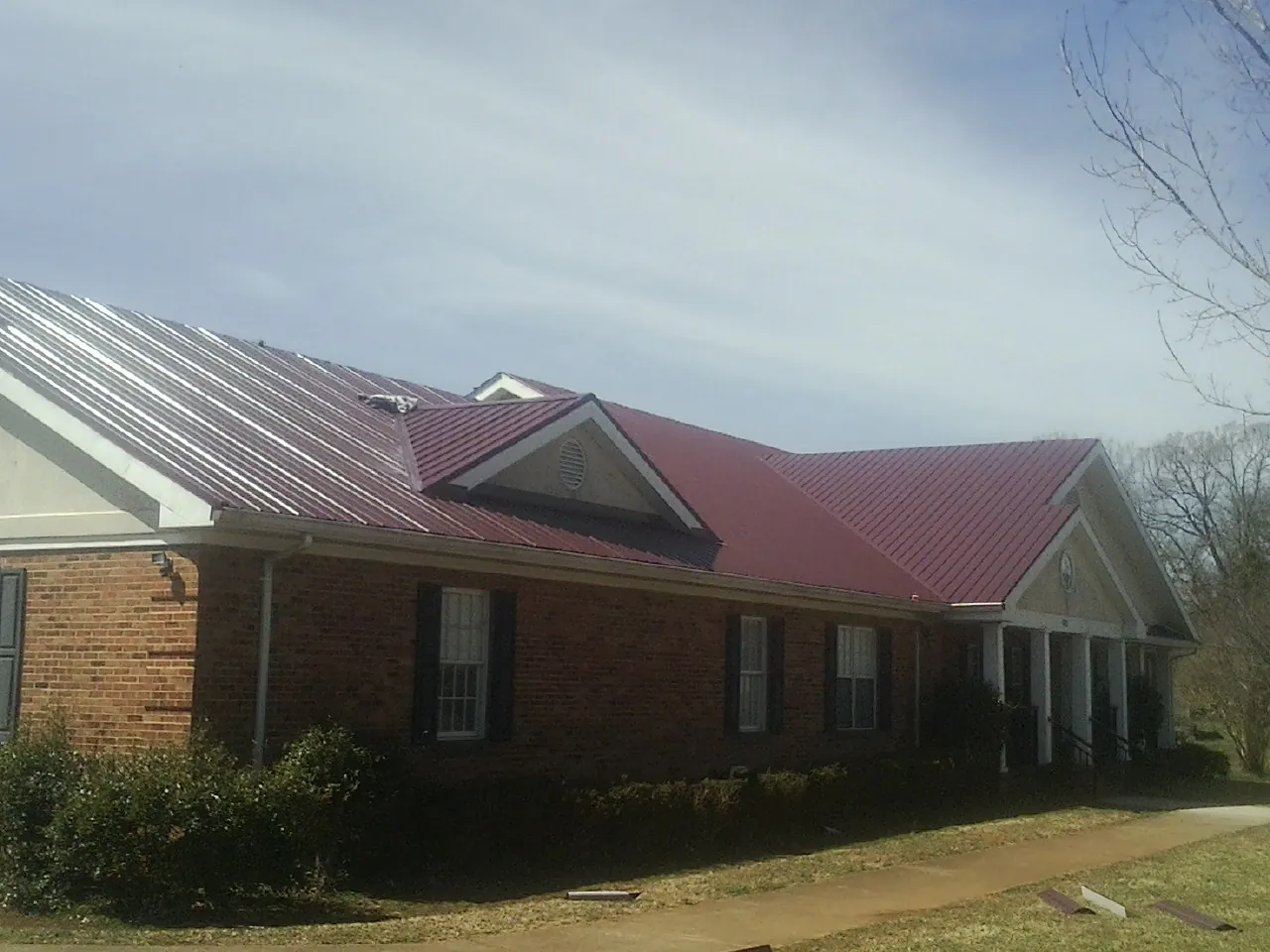 Red metal roof with gabled entries on a long brick building, from a Hail Damage Roof Repair job in Shortsville