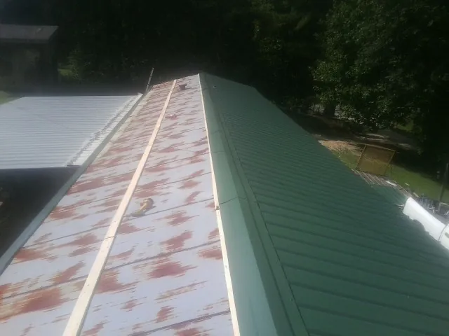 Old rusted panels beside newly installed green metal roofing — Wind Damage Roof Repair by Roofing Brothers in Shortsville