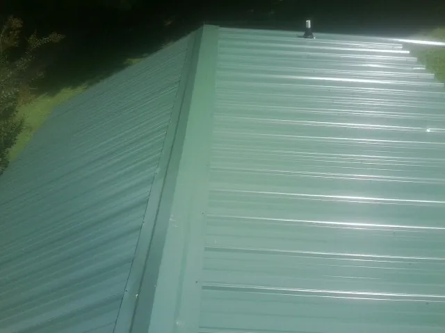 New green metal panels meeting at the ridge of a roof — Flat Roof Repair work by our crew in Shortsville