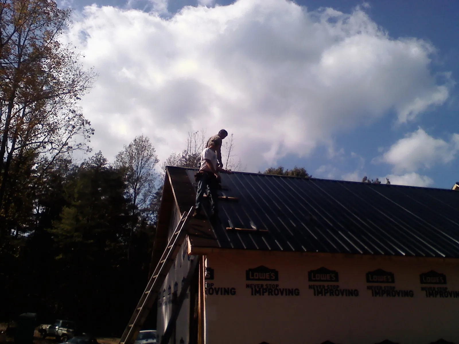 Roofer fastening dark metal panels high against a cloudy sky, from a Roof Inspection job in Shortsville