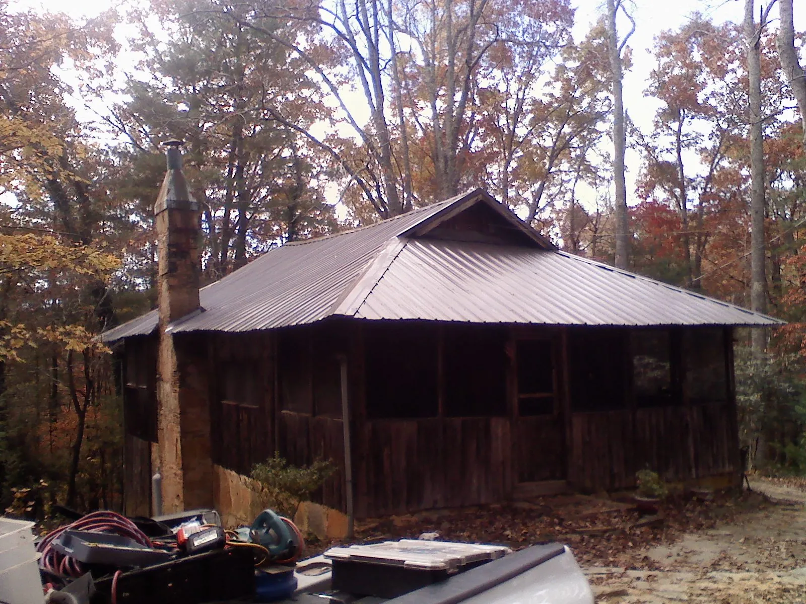 Brown metal hip roof on an old cabin with a stone chimney in Shortsville