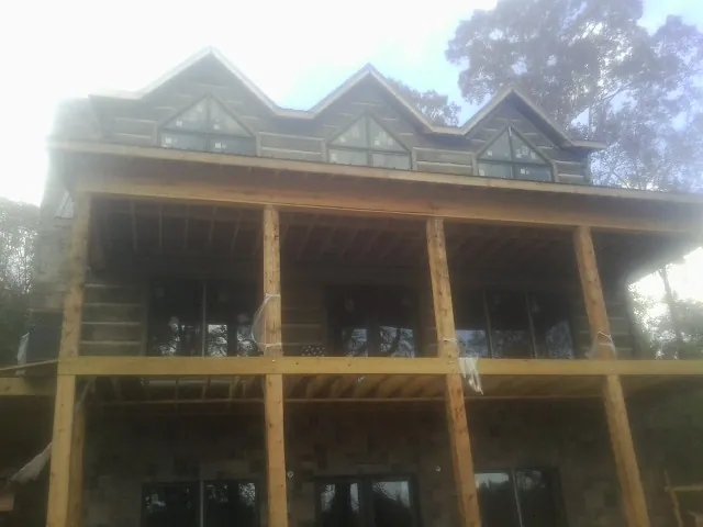 Dormers and porch framing on a large log home under construction — Roof Coating work by our crew in Shortsville