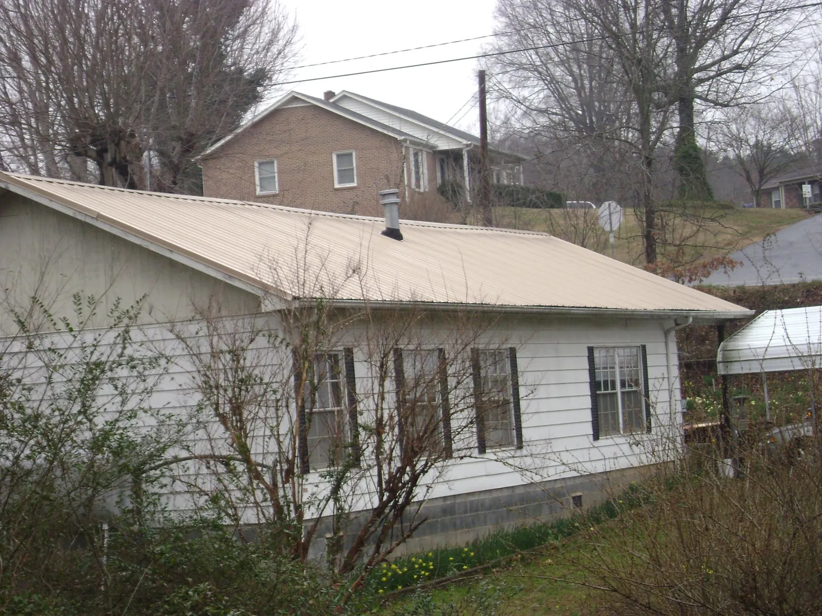 Tan metal roof on a white sided house set into a hillside — Commercial Roofing by Roofing Brothers in Shortsville