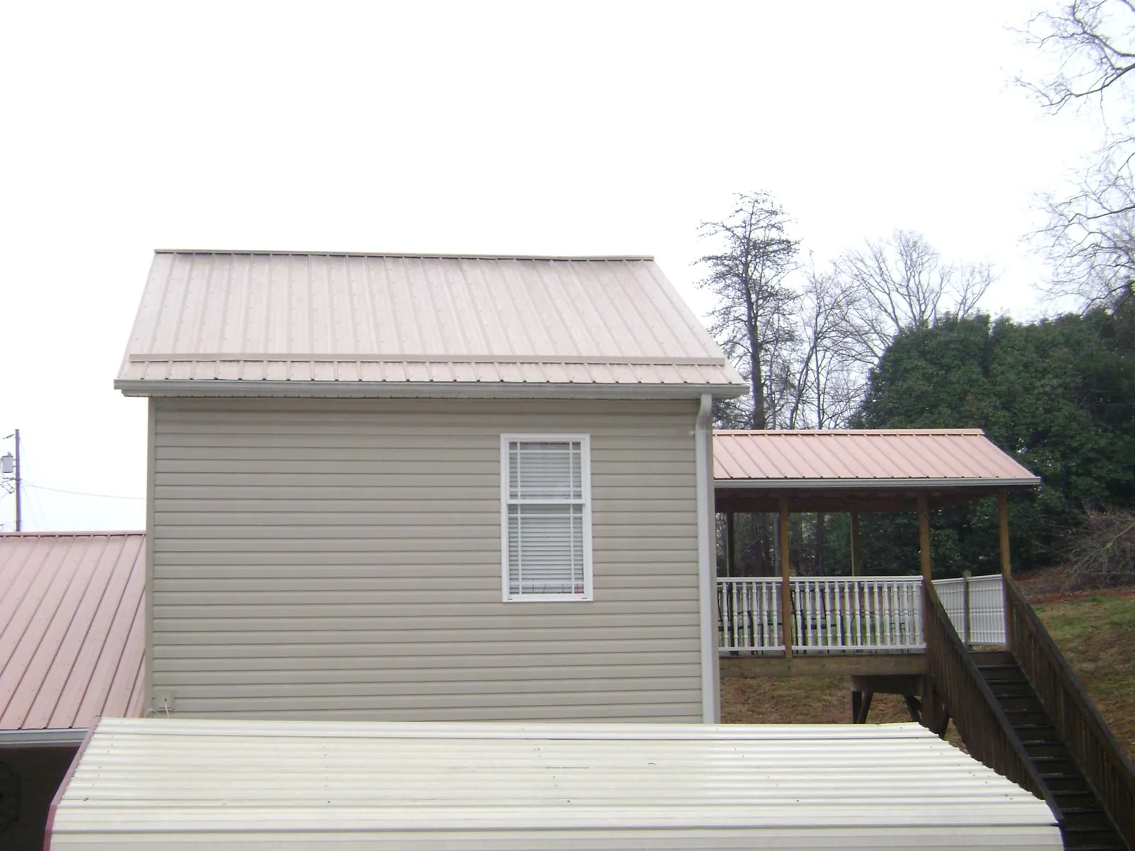 Tan metal roofs on a two story addition and attached porch, from a Roof Replacement job in Shortsville